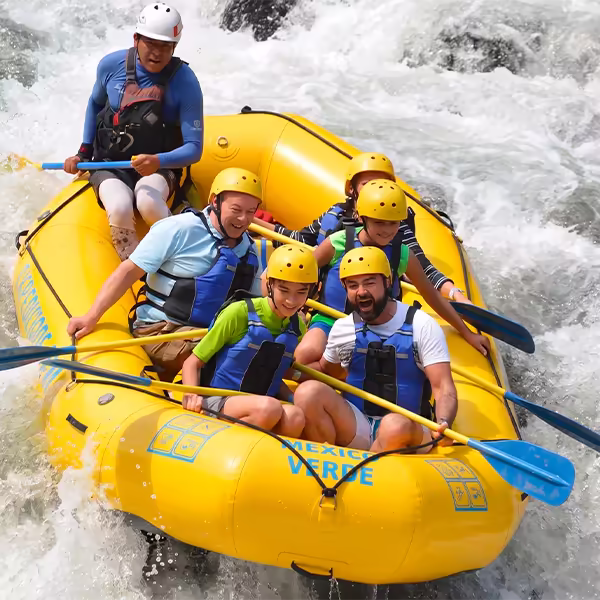 Un grupo de seis turistas sonrientes y un guía profesional en una balsa amarilla de rafting, Jalcomulco