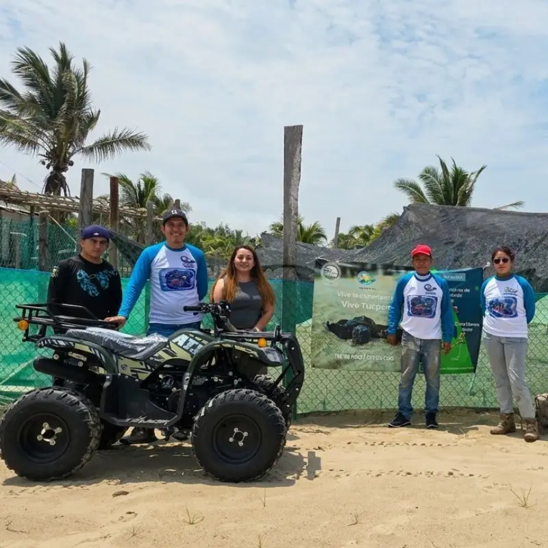 Equipo de voluntarios y fundadores del Campamento Tortuguero Mar de Plata posando sonrientes junto a una cuatrimoto de patrullaje y lonas informativas frente al corral de incubación en la playa de Tuxpan, Veracruz.