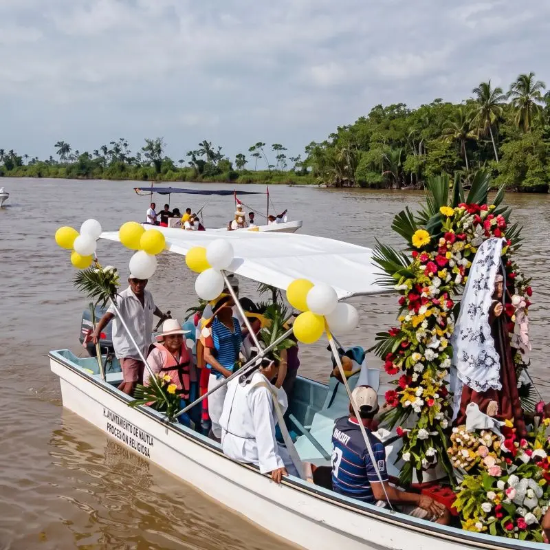 Procesión religiosa en lancha decorada con flores y globos sobre el río durante una fiesta patronal en la región de Gutiérrez Zamora, Veracruz.