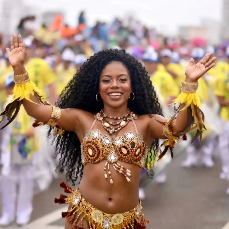 Mujer sonriente bailando con un traje festivo de cuentas y plumas durante un desfile del Carnaval de Tamiahua, Veracruz, con una multitud de personas celebrando al fondo.