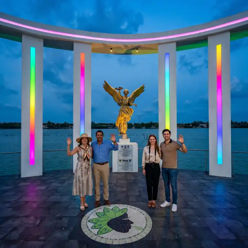 Cuatro turistas saludando frente al monumento del Ángel dorado iluminado con luces de colores durante el Carnaval de Tamiahua Veracruz.