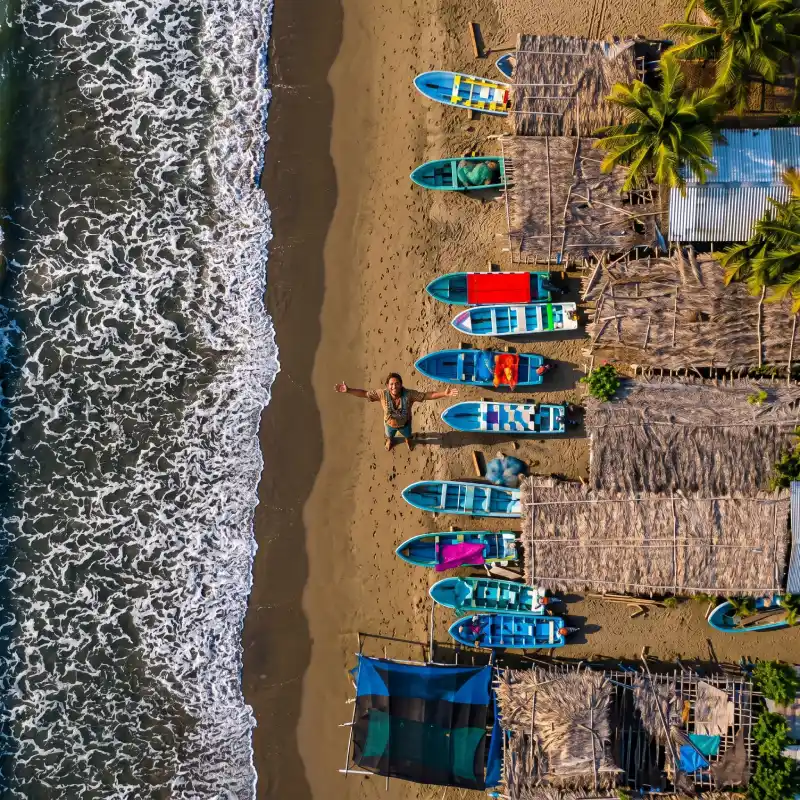Vista aérea de un hombre con los brazos abiertos en la arena junto a lanchas pesqueras y el oleaje tranquilo de la playa de Tamiahua Veracruz.