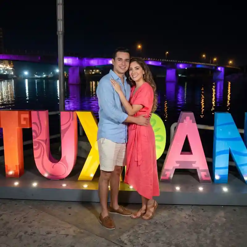 Pareja sonriendo junto a las letras monumentales de Tuxpan Veracruz iluminadas de noche en el malecón, reflejando el ambiente nocturno y los lugares turísticos en Tuxpan.