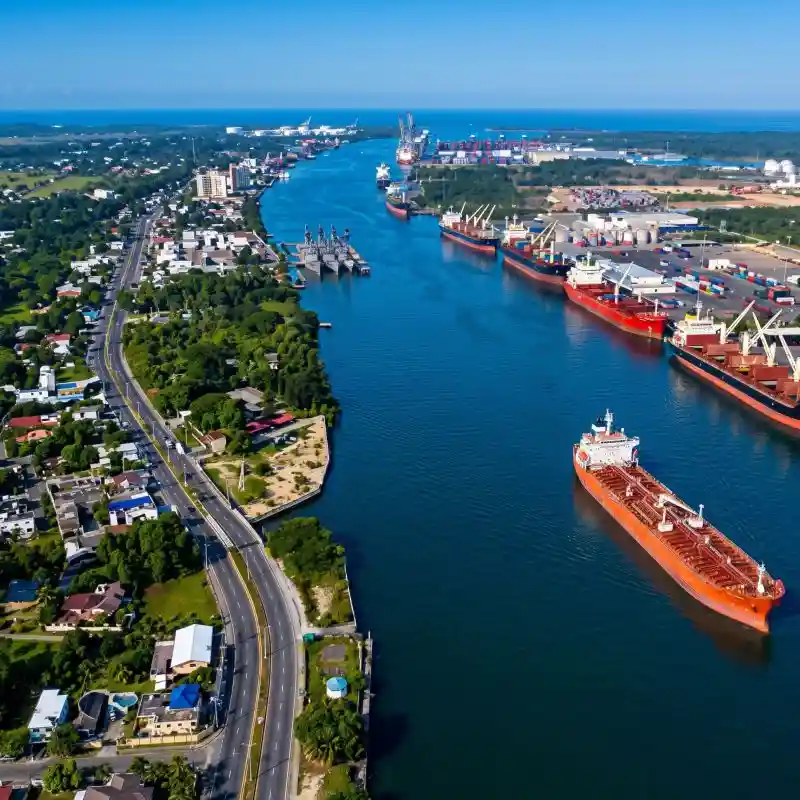 Vista aérea panorámica con dron del majestuoso Río Tuxpan Veracruz, mostrando grandes embarcaciones comerciales junto al puerto y el bulevar costero rodeado de vegetación.
