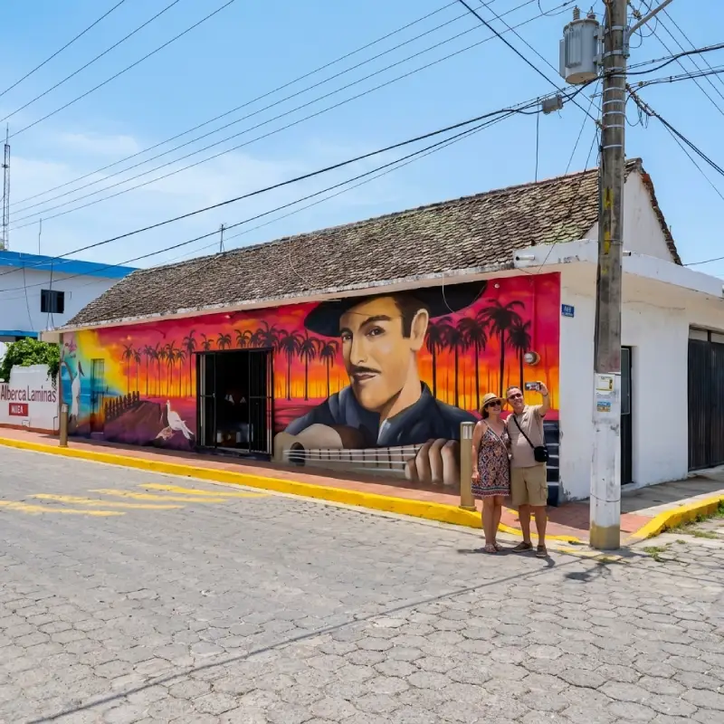 Pareja de turistas tomándose una selfie frente a un colorido mural callejero de un músico tradicional veracruzano en Nautla.