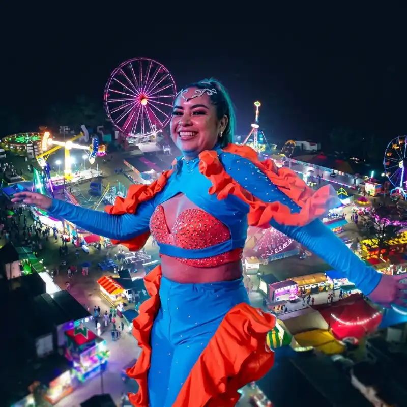 Vista nocturna de la Expoferia Tuxpan Veracruz con juegos mecánicos iluminados, una rueda de la fortuna y una bailarina sonriente en primer plano.