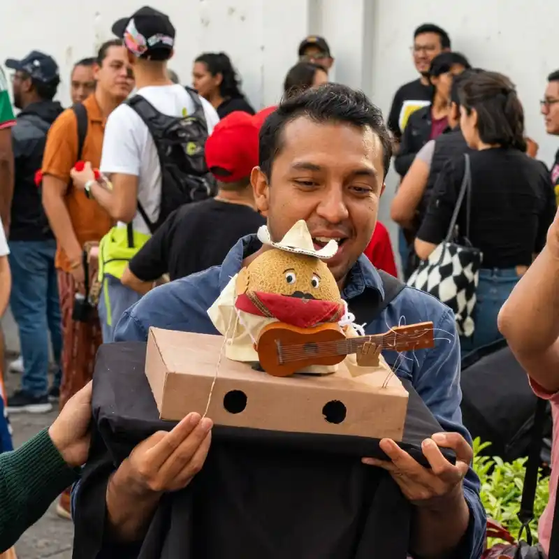 Participante mostrando un melón caracterizado con sombrero y guitarra miniatura para la Carrera de Melones en el Barrio Mágico de Xallitic, Xalapa.