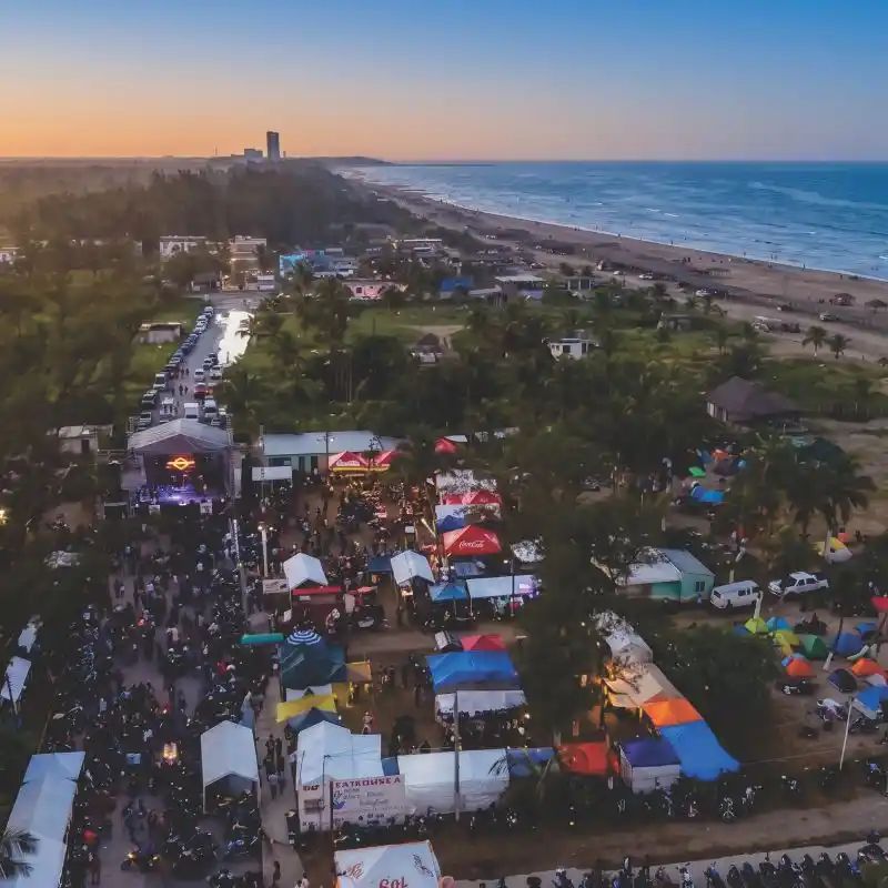 Vista aérea panorámica al atardecer de un concierto masivo y zona de campamento junto a la playa en Tuxpan Veracruz durante un evento de motos y autos.