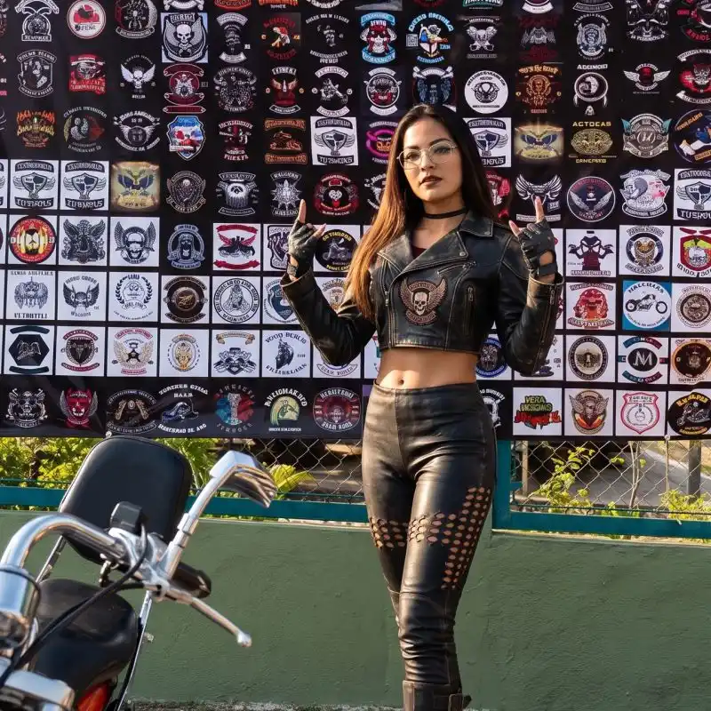 Joven motociclista con chamarra y pantalón de piel posando frente a un telón con parches y distintivos de rodadas durante el Motofest en Tuxpan Veracruz.