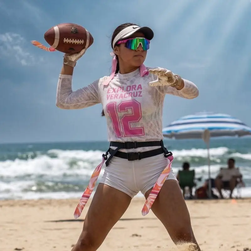 Atleta equipada con cinturón de banderas preparándose para lanzar un balón de americano durante un torneo de tocho playero en Tuxpan Veracruz.