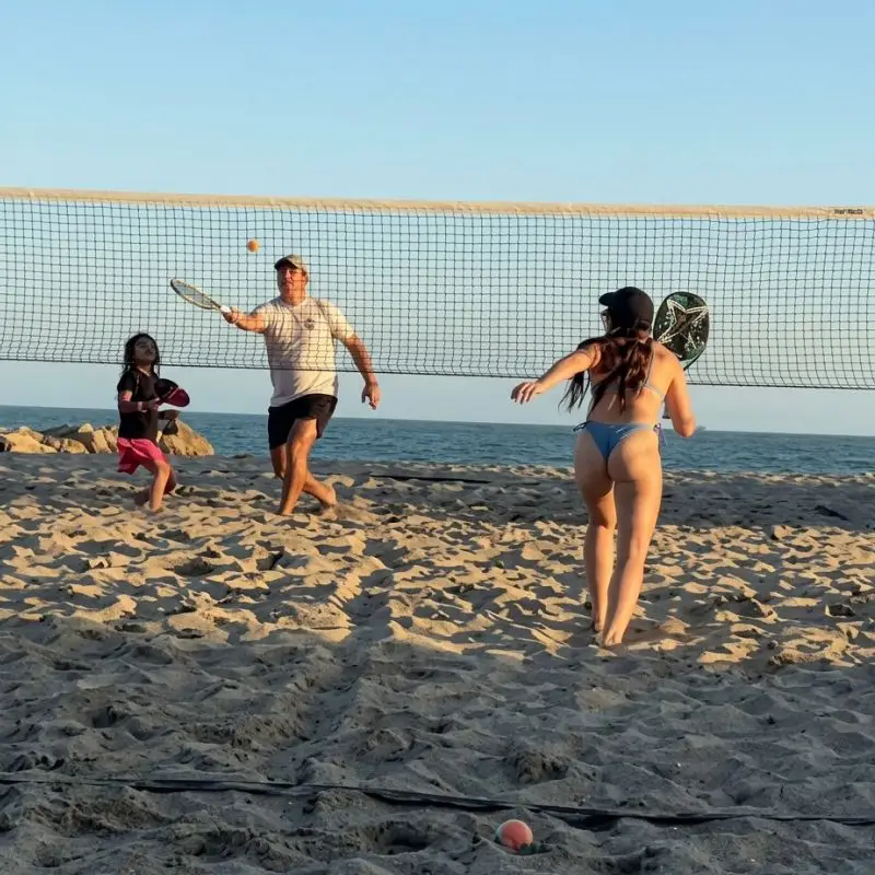 Familias y deportistas practicando tenis de playa en la arena de la costa de Tuxpan Veracruz, con la red y el mar al fondo durante la tarde.