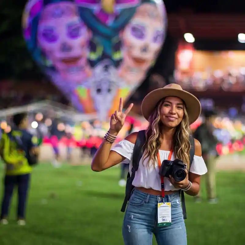 Joven turista con cámara fotográfica sonriendo frente a un enorme globo de papel iluminado en el Festival Internacional del Globo en San Andrés Tuxtla, un evento espectacular para el turismo en Veracruz.