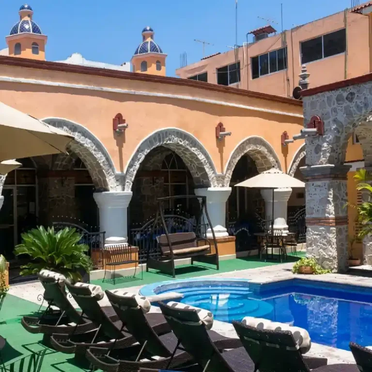 Patio colonial del Hotel Tajín Papantla con alberca, camastros, arquería de piedra, bancas de descanso y cúpulas azulejadas.