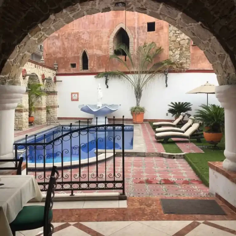 Alberca al aire libre del Hotel Tajín Papantla con reja de herrería, camastros, fuente decorativa y patio rústico veracruzano.