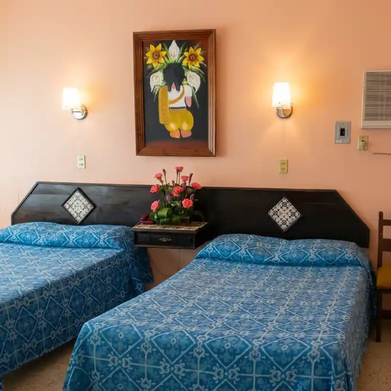 Habitación Doble Ejecutiva en Hotel Tajín Papantla con dos camas matrimoniales en tonos azules, cabecera de madera y cuadro decorativo.