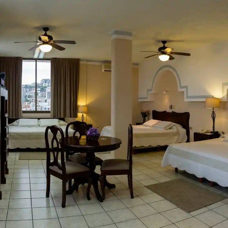 Interior de la Suite Presidencial en Hotel Tajín Papantla con amplio comedor de madera, múltiples camas y vista panorámica a la ciudad.