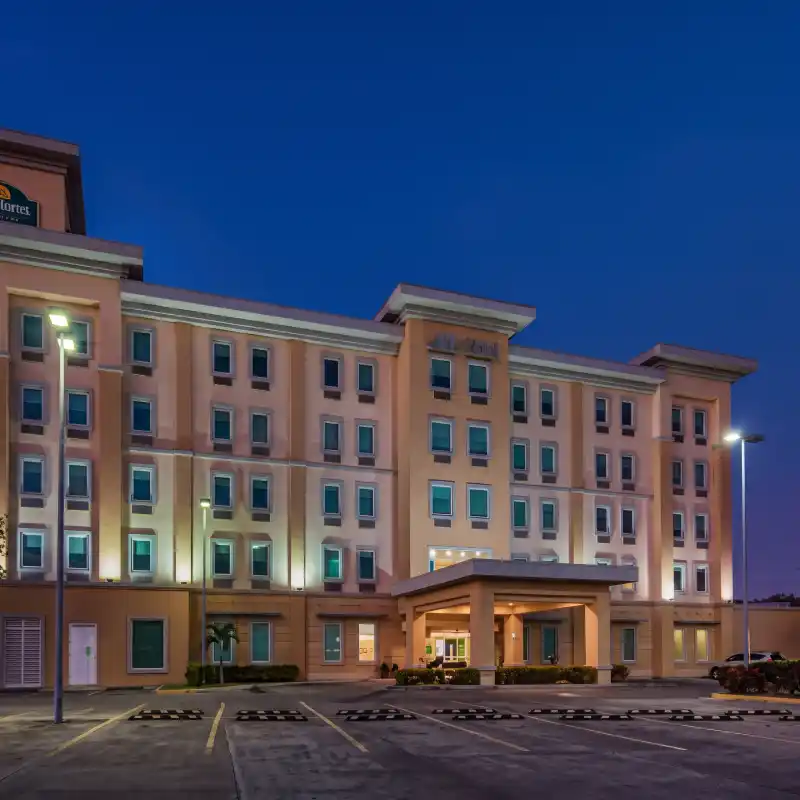 Fachada nocturna iluminada del Hotel La Quinta by Wyndham Poza Rica, destacando su amplio estacionamiento gratuito y seguro, ideal para vehículos y flotillas corporativas.