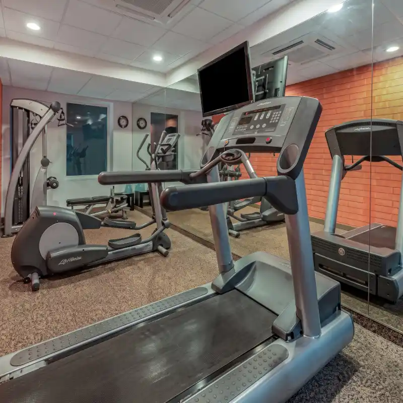 Moderno gimnasio equipado con caminadoras, elípticas y pantallas en el Hotel La Quinta by Wyndham Poza Rica, ideal para mantener rutinas de ejercicio durante viajes corporativos.