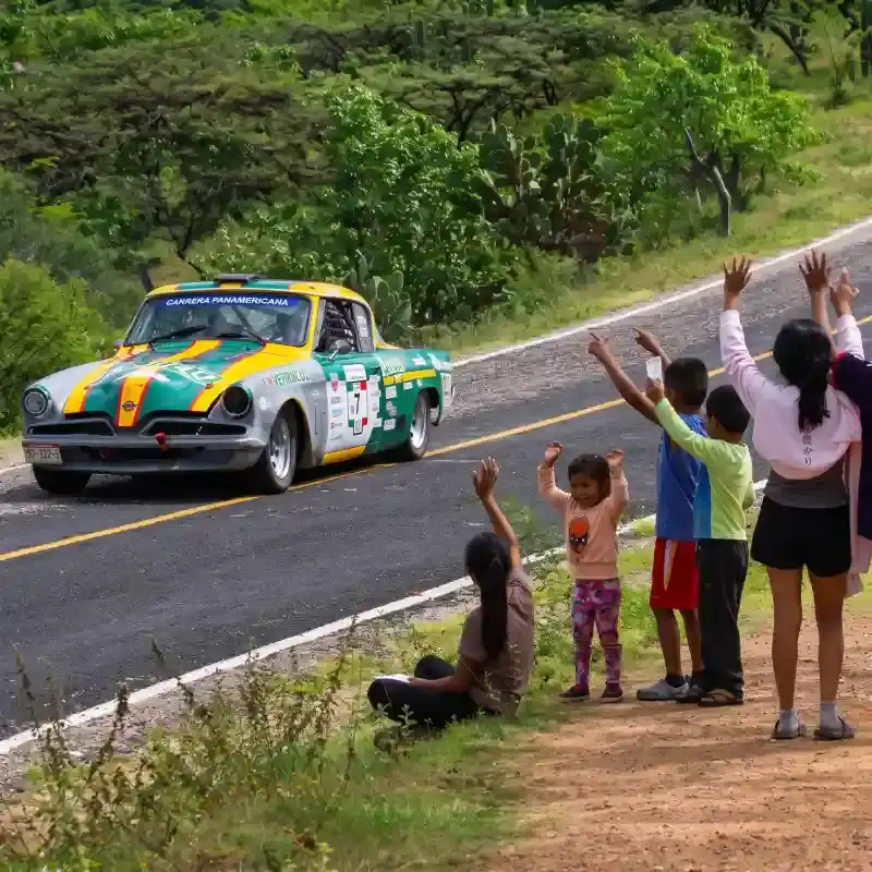 Niños y habitantes de una comunidad rural saludando con emoción al auto clásico de competencia durante el paso de La Carrera Panamericana en Veracruz.