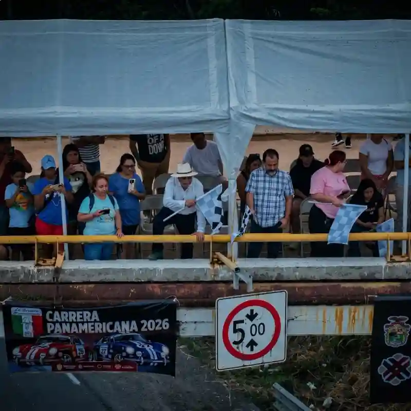 Organizadores y espectadores con banderas de cuadros en una zona de meta durante La Carrera Panamericana en Minatitlán, impulsando la ocupación hotelera.