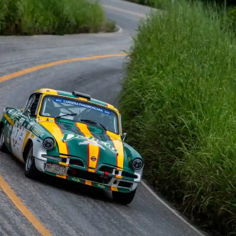Auto clásico de competencia tomando una curva cerrada rodeado de abundante vegetación durante el espectáculo en las curvas de La Carrera Panamericana.
