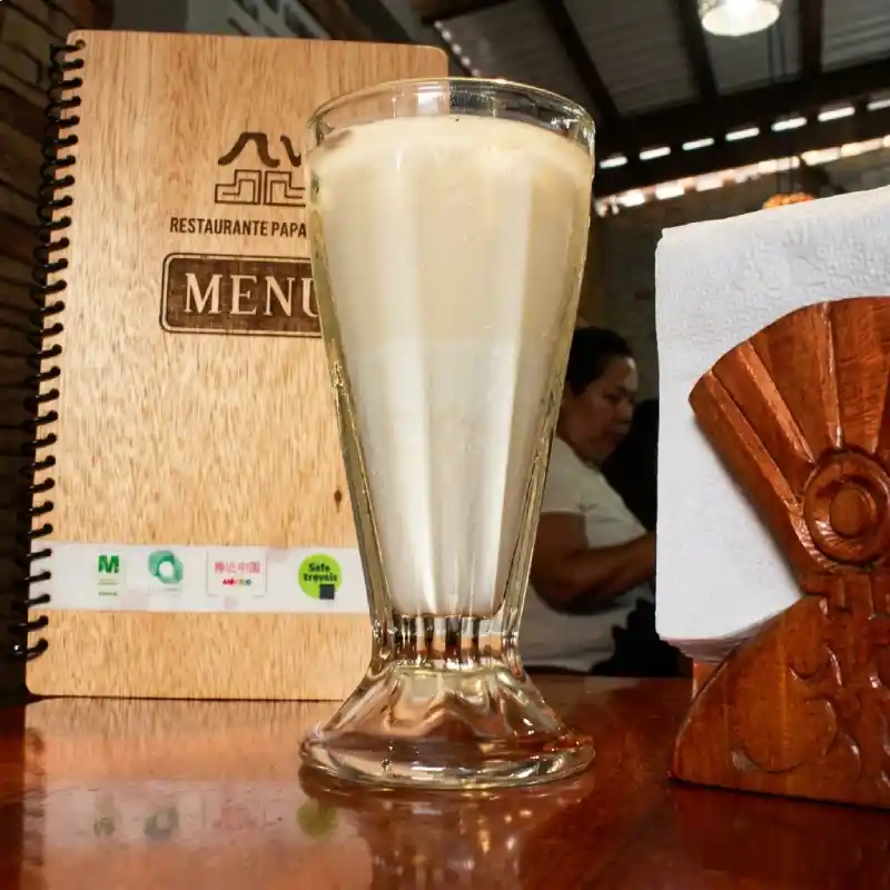 Bebida artesanal de vainilla natural en vaso de cristal junto al menú impreso en madera de Restaurante Nakú, tradición gastronómica del Alma Totonaca en Explora Veracruz.