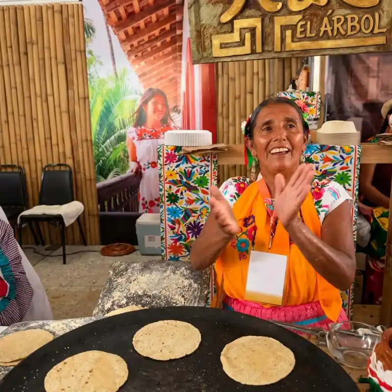 Cocinera tradicional de las Mujeres de Humo palmeando y cociendo tortillas de maíz hechas a mano en comal para Restaurante Nakú, orgullo del Alma Totonaca en Explora Veracruz.