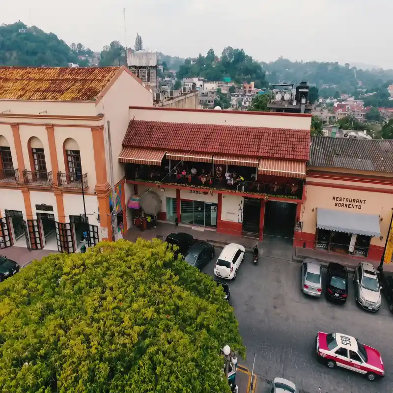 Toma aérea de la fachada del Restaurante Plaza Pardo en Papantla mostrando la zona de estacionamiento vehicular a nivel de calle frente al Zócalo.