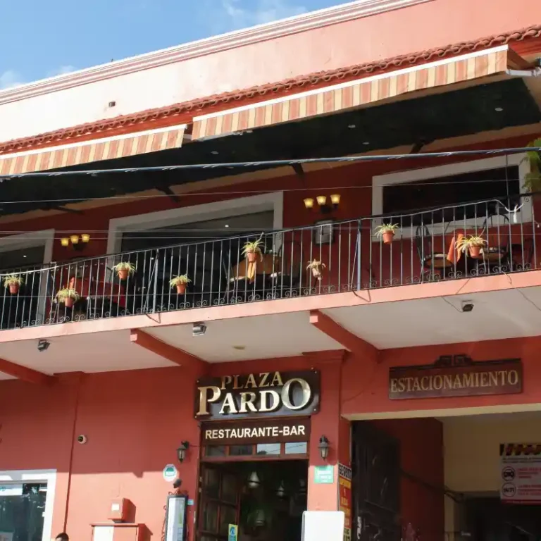 Fachada colonial en color terracota del Restaurante-Bar Plaza Pardo en el centro de Papantla, Veracruz, mostrando el letrero principal, la entrada al estacionamiento y la balconada superior decorada con macetas.