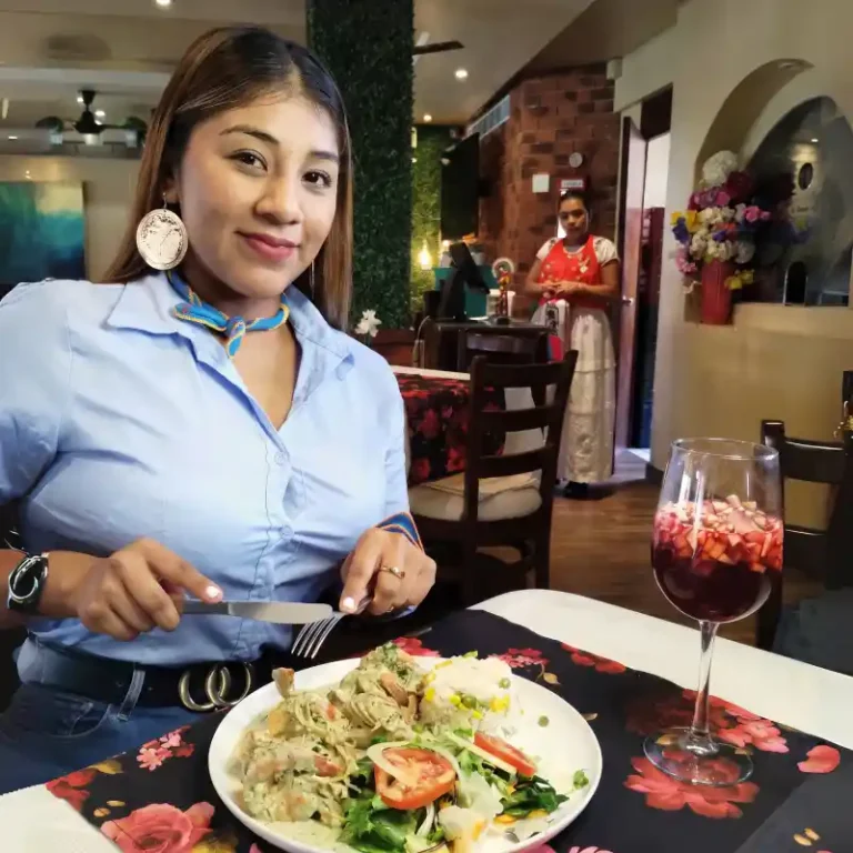Comensal disfrutando de un platillo gourmet y una copa de sangría en el salón interior climatizado del Restaurante Plaza Pardo en Papantla, con personal luciendo vestimenta tradicional de fondo.